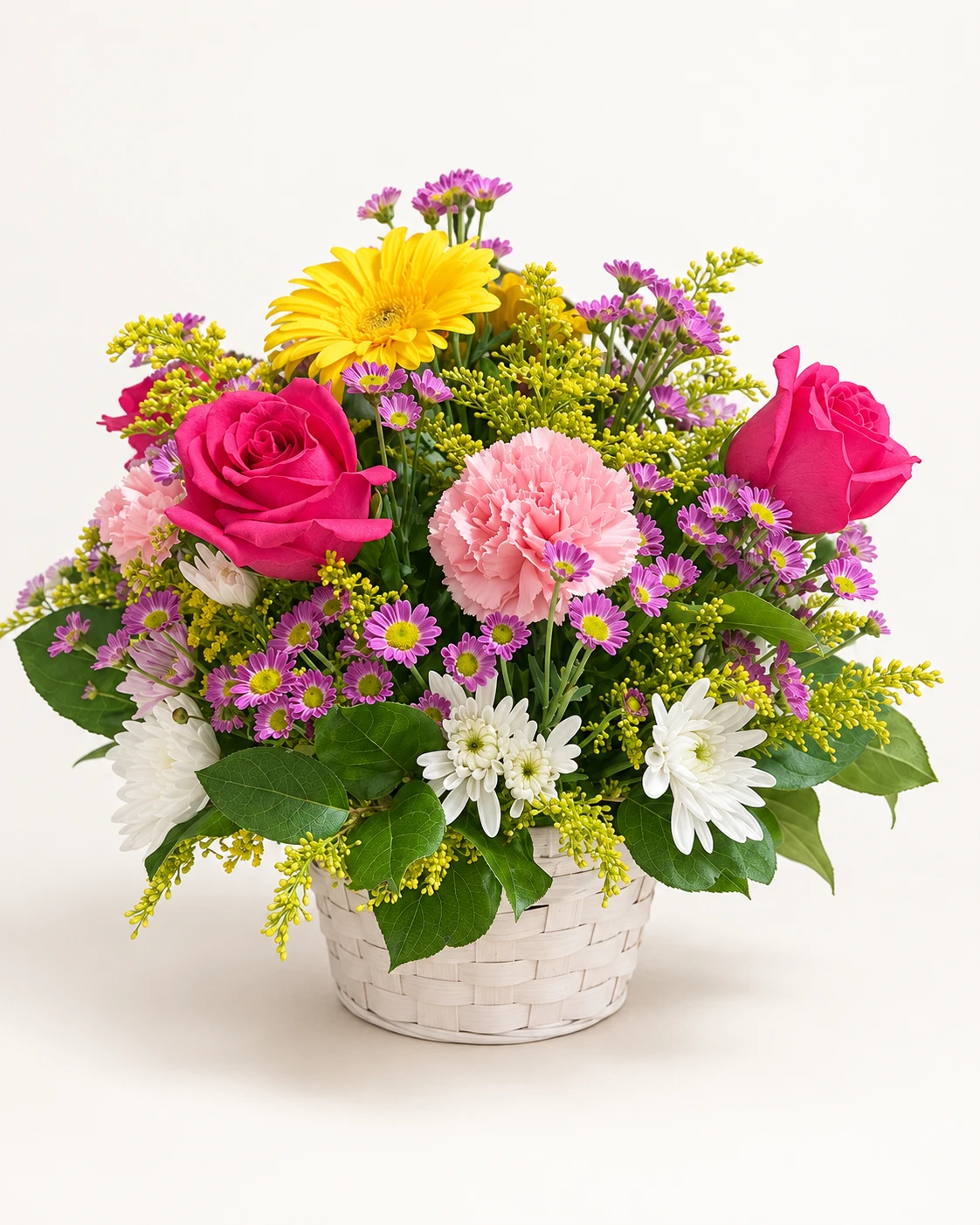 Canasta blanca con rosas fucsias, gerbera amarilla, claveles rosados y flores pequeñas moradas y blancas