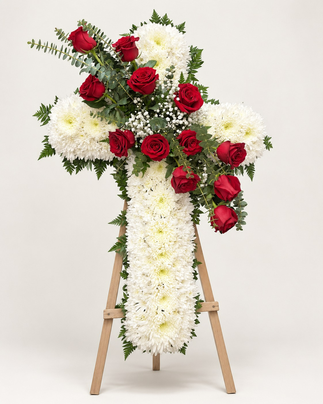 Cruz floral fúnebre blanca con rosas rojas sobre atril