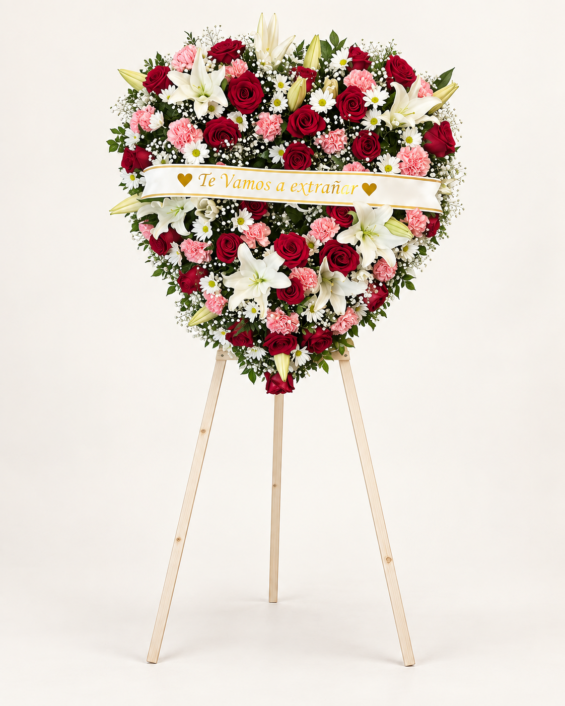 Arreglo fúnebre 1: corona en forma de corazón con rosas rojas, claveles rosados, lirios blancos y listón «Te Vamos a Extrañar» sobre atril