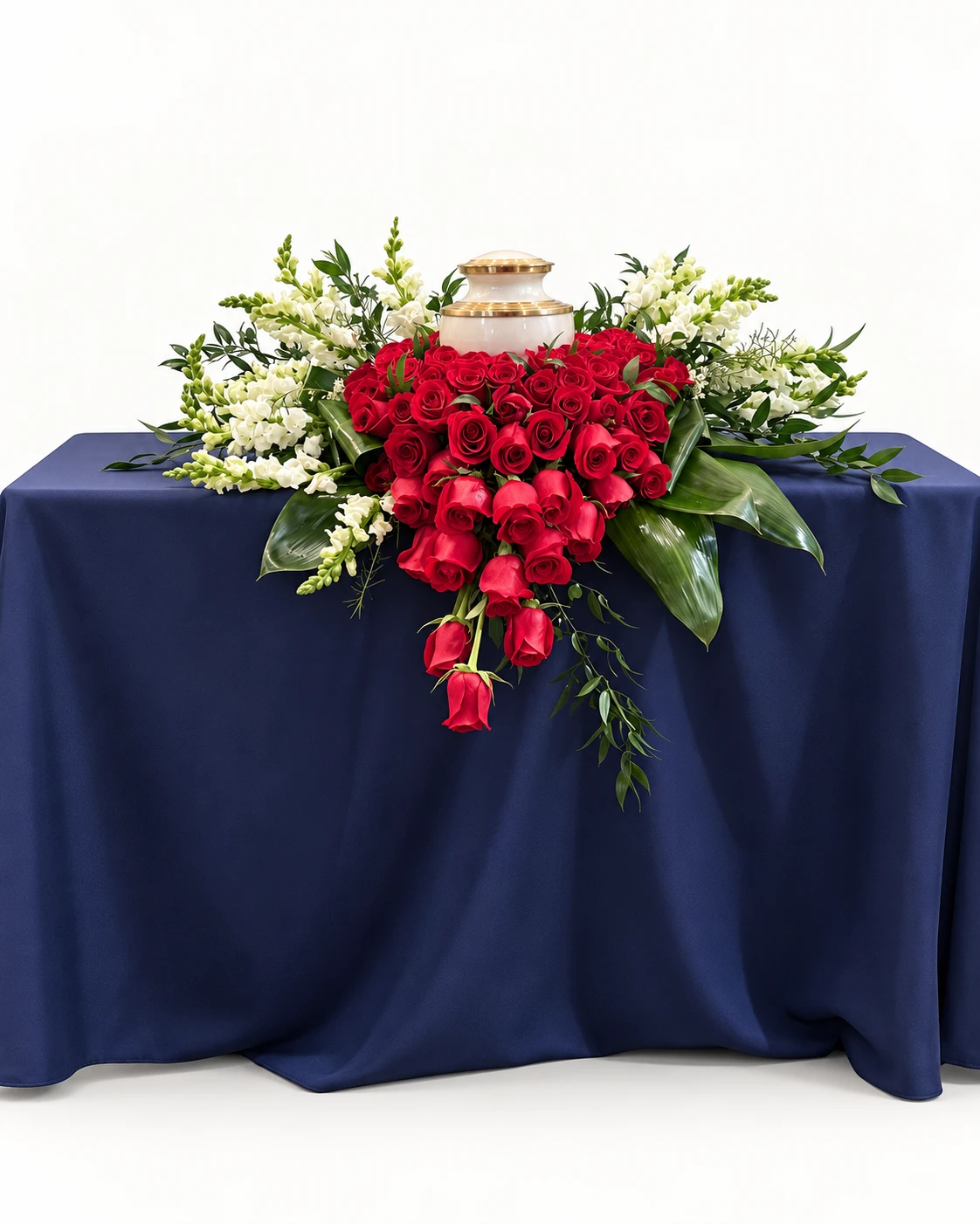 Arreglo floral para urna con rosas rojas, flores blancas y follaje verde sobre mesa con mantel azul